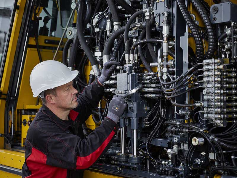 A professional engineer performing hydraulic system troubleshooting and preventive maintenance on a complex industrial machine to reduce lifecycle costs.