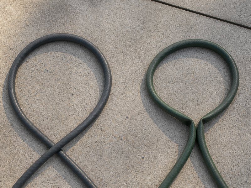 Two garden hoses bent into the same tight loop on a driveway, the polyurethane hose holding an open round curve while the rubber hose has collapsed into a flat kink
