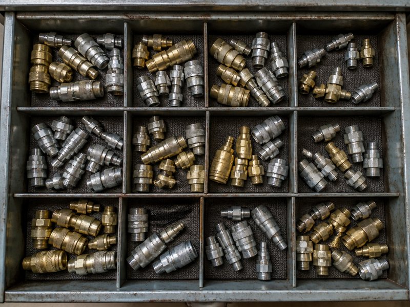 Workshop drawer of mismatched air tool coupler types with adapters, showing the inventory cost of a mixed coupler standard